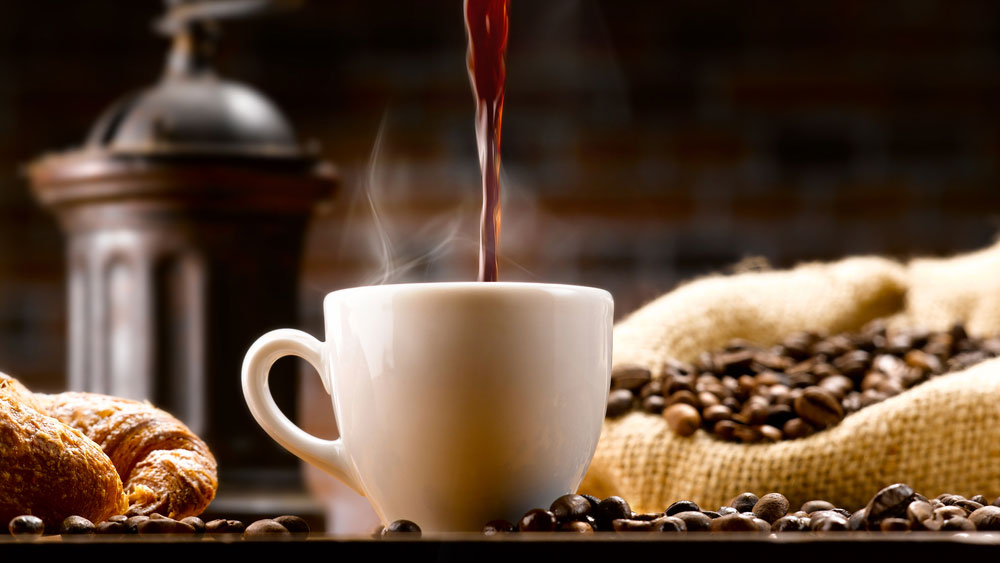 Tasse Kaffee im Setting zwischen Kaffeebohnen und Kaffeemühle